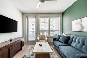 Ein Wohnzimmer mit Flachbildfernseher, einer Couch, einem Couchtisch und einem Sessel.