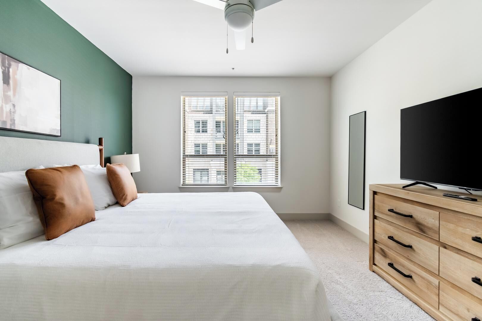 Ein Schlafzimmer mit Bett, Fernseher, Kommode und einem Fenster mit Jalousien.