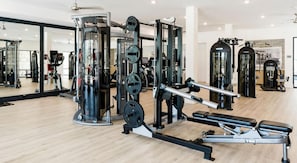 Ein Fitnessraum mit unterschiedlichen Trainingsgeräten, Spiegeln und einem Holzboden.