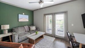 A living room with a sofa, coffee table, and a TV. - Landing | Spectacular 2BD, Pool, Gym (Nashville)