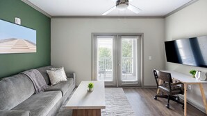 A living room with a grey sofa, a coffee table, a TV, and a ceiling fan. - Landing | Spectacular 2BD, Pool, Gym (Nashville)
