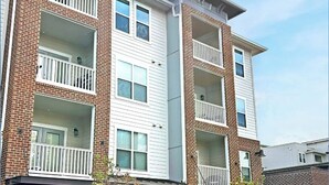 A multi-story apartment building with balconies, a ground-level entrance, and a sign indicating the building is open. - Landing | Beautiful 2BD, Gym, Pool (Nashville)