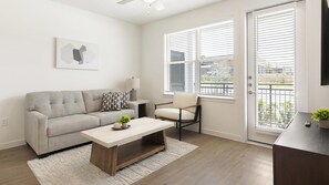 A modern living room with a sofa, a chair, a coffee table, and a TV. - Landing | Chic 1BD, Pool, Gym (Dallas)