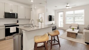 Cocina moderna con una isla central, electrodomésticos de acero inoxidable y una zona de comedor con sofá y sillas.