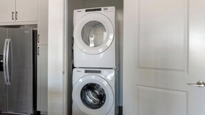 Ein kleiner Hauswirtschaftsraum mit einer übereinander angeordneten Waschmaschine und einem Trockner, einem Edelstahlkühlschrank und weißen Schränken.