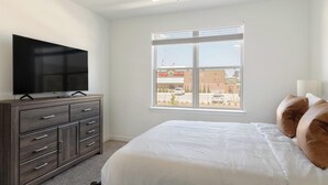 Een slaapkamer met een bed, een televisie op een dressoir en een raam met uitzicht op een gebouw.