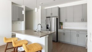 A modern kitchen with grey cabinets, stainless steel appliances, and a central island with bar stools. - Landing | Beautiful 2BD, Courtyard, Gym (Dallas)