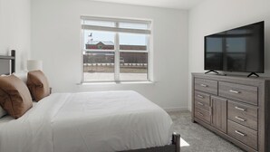 A bedroom with a bed, a dresser, a television, and a window with a view of a building and a flag. - Landing | Beautiful 2BD, Courtyard, Gym (Dallas)