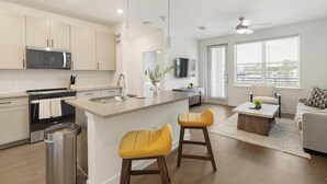 Una cocina moderna con una isla central, una zona de comedor con sofá y sillas, y un gran ventanal con persianas.
