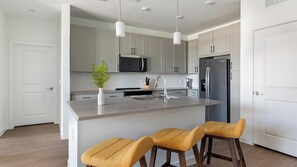 A modern kitchen with a central island, stainless steel appliances, and a white tiled backsplash. - Landing | Amazing 1BD, Courtyard, Gym (Dallas)