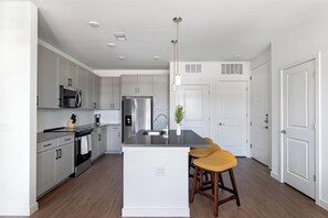 A modern kitchen with a central island, stainless steel appliances, and a white color scheme. - Landing | Spectacular 1BD, Gym, Pool (Dallas)