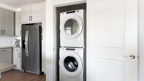 A compact kitchen with a stainless steel refrigerator, a built-in washer and dryer, and white cabinetry. - Landing | Amazing 1BD, Courtyard, Gym (Dallas)