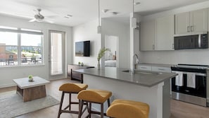 A modern kitchen with a central island, bar stools, a microwave, and a stove. - Landing | Spectacular 1BD, Gym, Pool (Dallas)