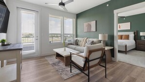 A modern living room with a sofa, coffee table, and a chair, a bed with a nightstand, and a ceiling fan. - Landing | Amazing 2BD, Gym, Clubhouse (San Antonio)