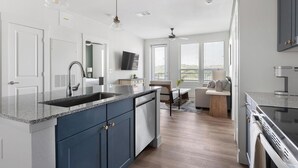 A modern kitchen with a granite countertop, built-in cabinets, a dishwasher, and a large window. - Landing | Amazing 2BD, Gym, Clubhouse (San Antonio)