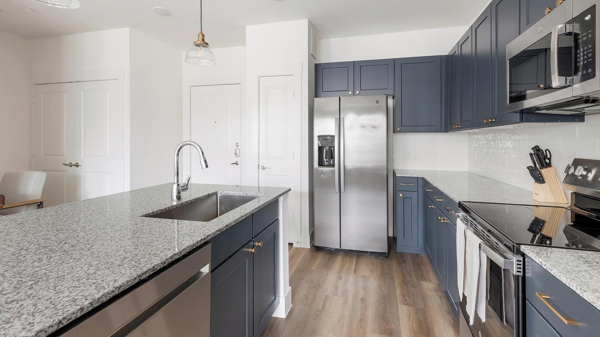 A modern kitchen with granite countertops, stainless steel appliances, and dark blue cabinetry.