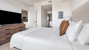 Quarto com uma cama, uma televisão sobre uma cômoda de madeira e uma porta que dá para o banheiro.