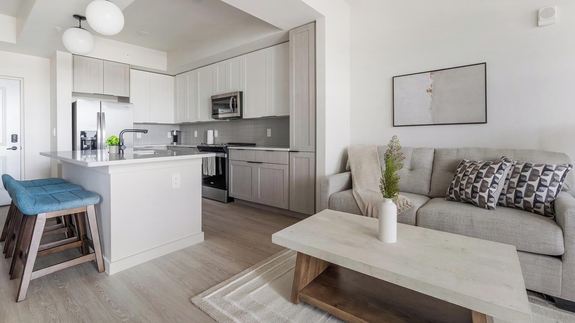 Une cuisine moderne avec des meubles blancs, un îlot central et un coin repas agrémenté d’une chaise bleue.