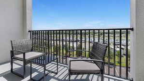 Een balkon met twee rieten stoelen en een tafel, met uitzicht op een parkeerplaats en een wateroppervlak.