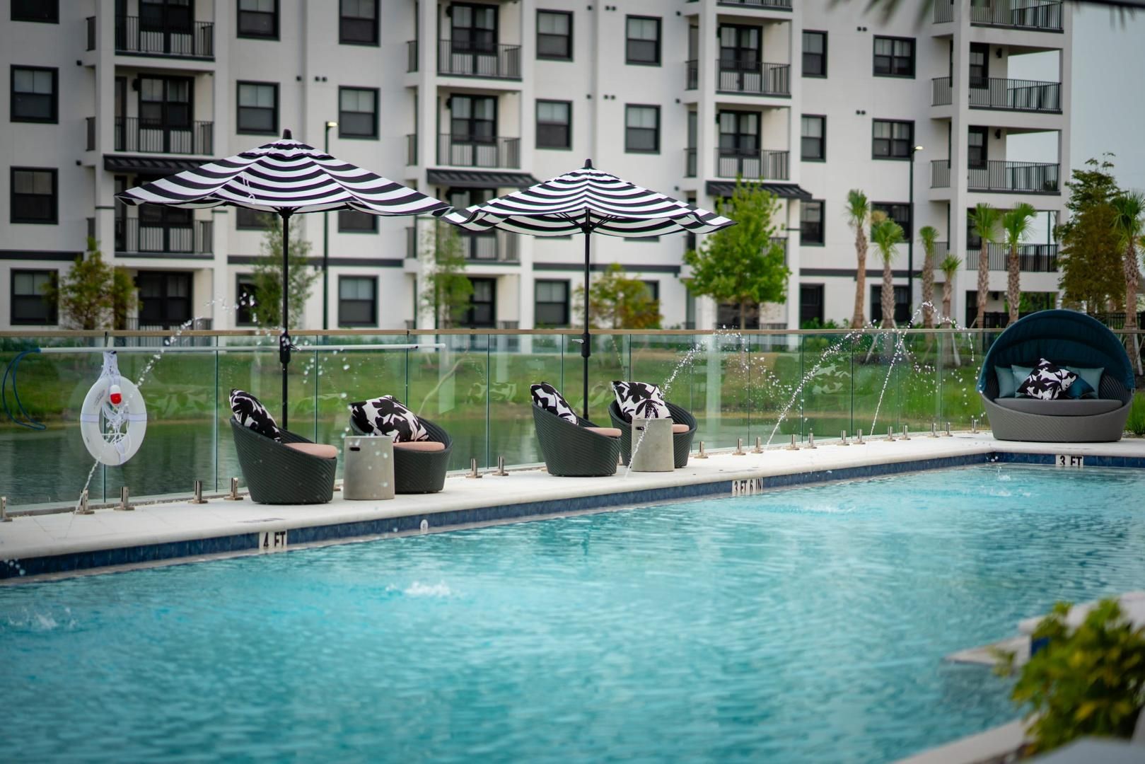 Een zwembad met ligbedden en parasols, omgeven door een glazen balustrade en een gebouw op de achtergrond.