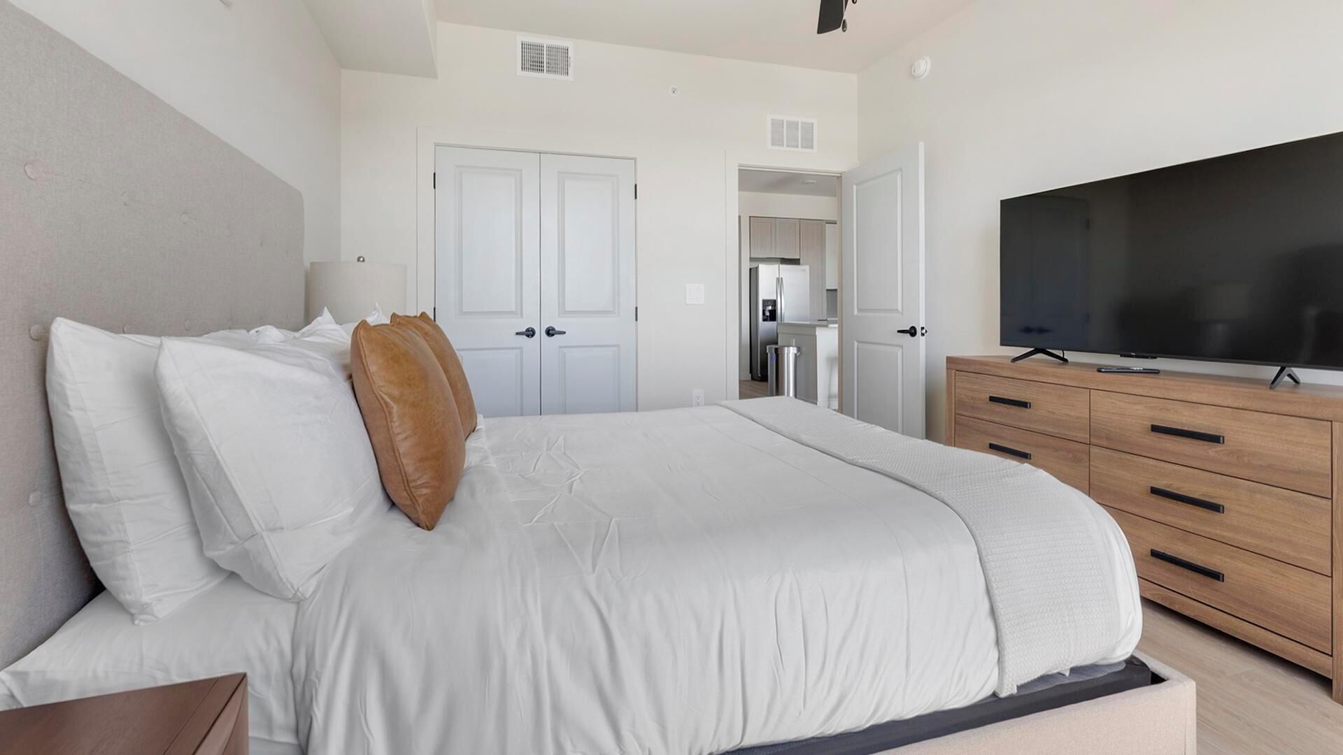 A bedroom with a bed, a TV, a dresser, and a door leading to a bathroom.