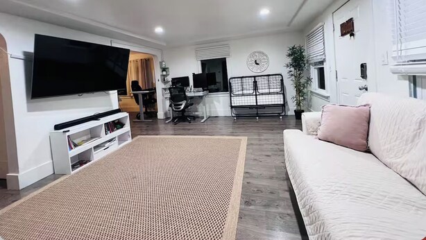 A modern living room with a flat-screen TV, a sofa, a coffee table, and a dining area with a chair and a small table.