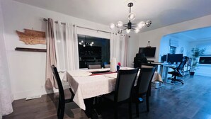 A dining area with a table set for four, a modern chandelier, and a view into the living room.