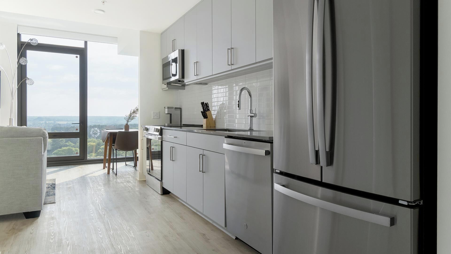 A modern kitchen with stainless steel appliances, a dining area with a view, and a large window.
