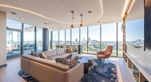 Ein modernes Wohnzimmer mit einer großen Couch, einem Couchtisch und Blick auf die Stadt durch große Fenster.