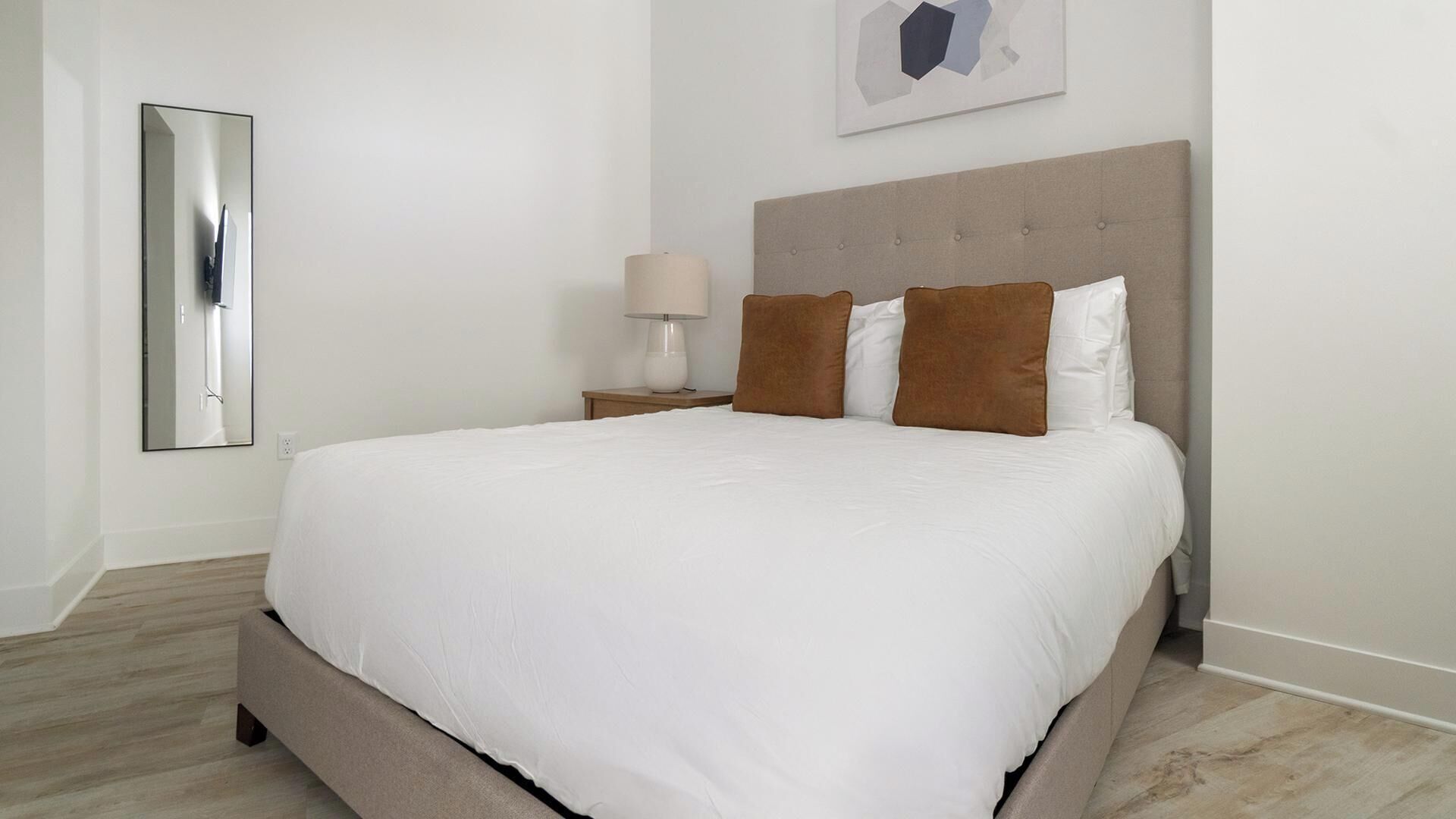 A hotel room with a large bed, a nightstand with a lamp, and a wall-mounted mirror.