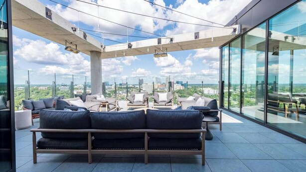 A modern lounge area with a sofa, chairs, and a glass wall offering a city view. - Landing | Incredible 1BD in Caraleigh (Raleigh)
