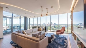 A modern living room with a large sofa, a coffee table, and a view of the cityscape through large windows. - Landing | Incredible 1BD in Caraleigh (Raleigh)
