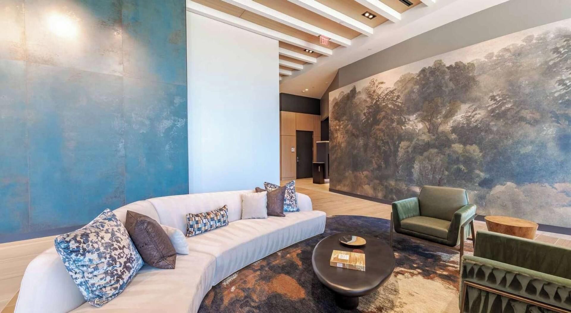A modern living room with a curved sofa, a green armchair, a round coffee table, and a large abstract mural on the wall.