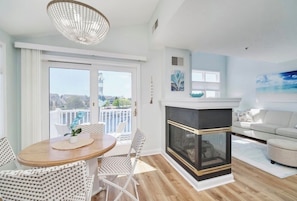 A modern living room with a fireplace, a dining area with a round table and chairs, and a balcony with a view. - Cozy 1-bedroom Pet Friendly Condo in Manistee.   Pool, Hot tub, 5 min to Beach! (Manistee)