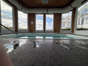 Ein Pool mit einer Holzterrasse und großen Fenstern.