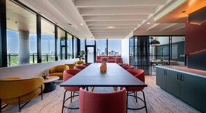 A modern conference room with a long table, red and yellow chairs, a city view, and a kitchen area. - Landing | Modern Studio in Caraleigh (Raleigh)