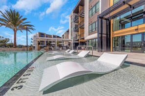 Ein moderner Poolbereich mit Liegestühlen, einer Palme und einem Gebäude mit großen Fenstern.