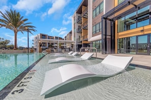 A modern hotel pool area with lounge chairs, a palm tree, and a building with large windows. - Landing | Stylish 1BD, Game Room, Pool (Largo)