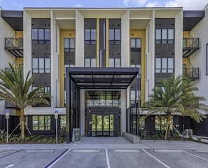 A modern building with a central entrance, multiple balconies, and a parking area. - Landing | Stylish 1BD, Game Room, Pool (Largo)
