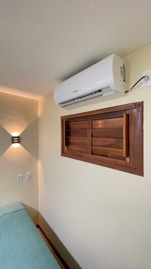 Habitació amb aire condicionat fixat a la paret, un panell de fusta sobre una finestra i una làmpada a la paret.