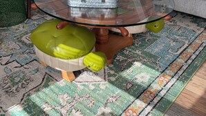 Un saló amb una taula de centre de vidre, un sofà, un moqueta amb dibuixos i un otomà verd.