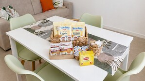Ruokailutila, jossa on valkoinen pöytä, vihreät tuolit ja kori täynnä ruokatarvikkeita.