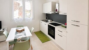Moderni keittiö, jossa on valkoiset kaapit, musta liesi ja ruokailutila, jossa on pöytä ja tuolit.