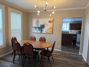 A dining area with a round table and six chairs, a ceiling light fixture, and a painting on the wall. - Sleeps 12 • King Bed • Near Zoo, Dundee & Blackstone (Omaha)