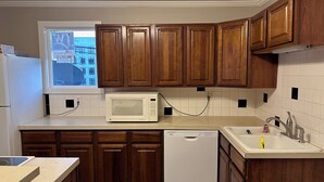 Cozinha com armários de madeira, micro-ondas branco, lava-louças e janela com vista para a cidade.