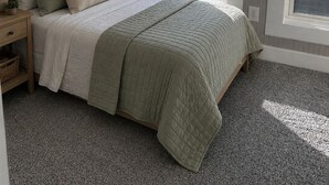 Quarto com cama, mesa de cabeceira, luminária e ventilador de teto.