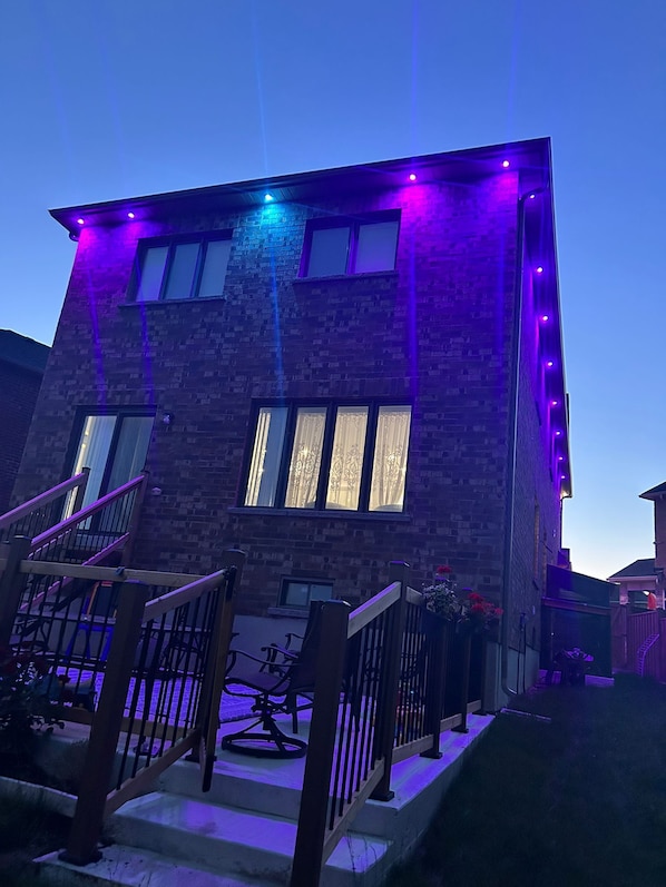 A two-story building with a brick facade, a visible staircase, and a window with curtains. - Luxury Niagara Retreat | 4 Bedrooms & 4 Washrooms | Designer Décor & Comfort (Thorold)