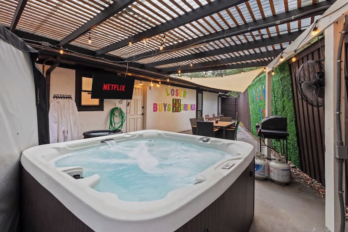 Una vasca idromassaggio in una zona patio esterna con una pergola sopra, un cartello Netflix e un muro con un cartello 'LOST'.