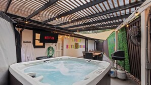 Ein Whirlpool in einem Außenbereich mit Patio, einer Pergola darüber, einem Netflix-Schild und einer Wand mit einem 'LOST'-Schild.