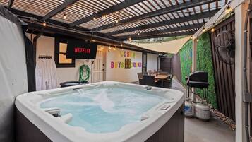 Una vasca idromassaggio in una zona patio esterna con una pergola sopra, un cartello Netflix e un muro con un cartello 'LOST'.